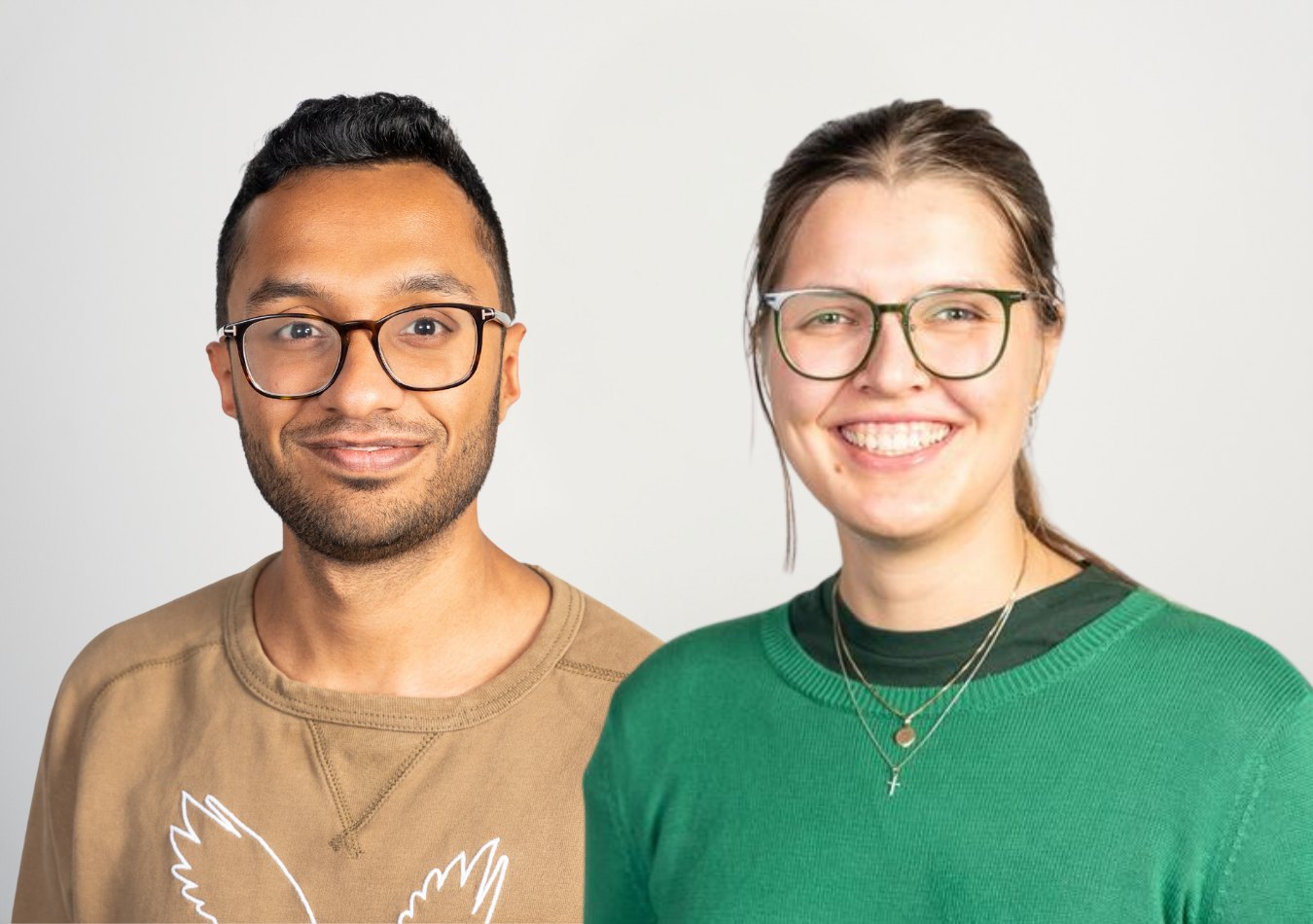 Zwei Personen vor hellem Hintergrund, beide mit Brille, lachen in die Kamera